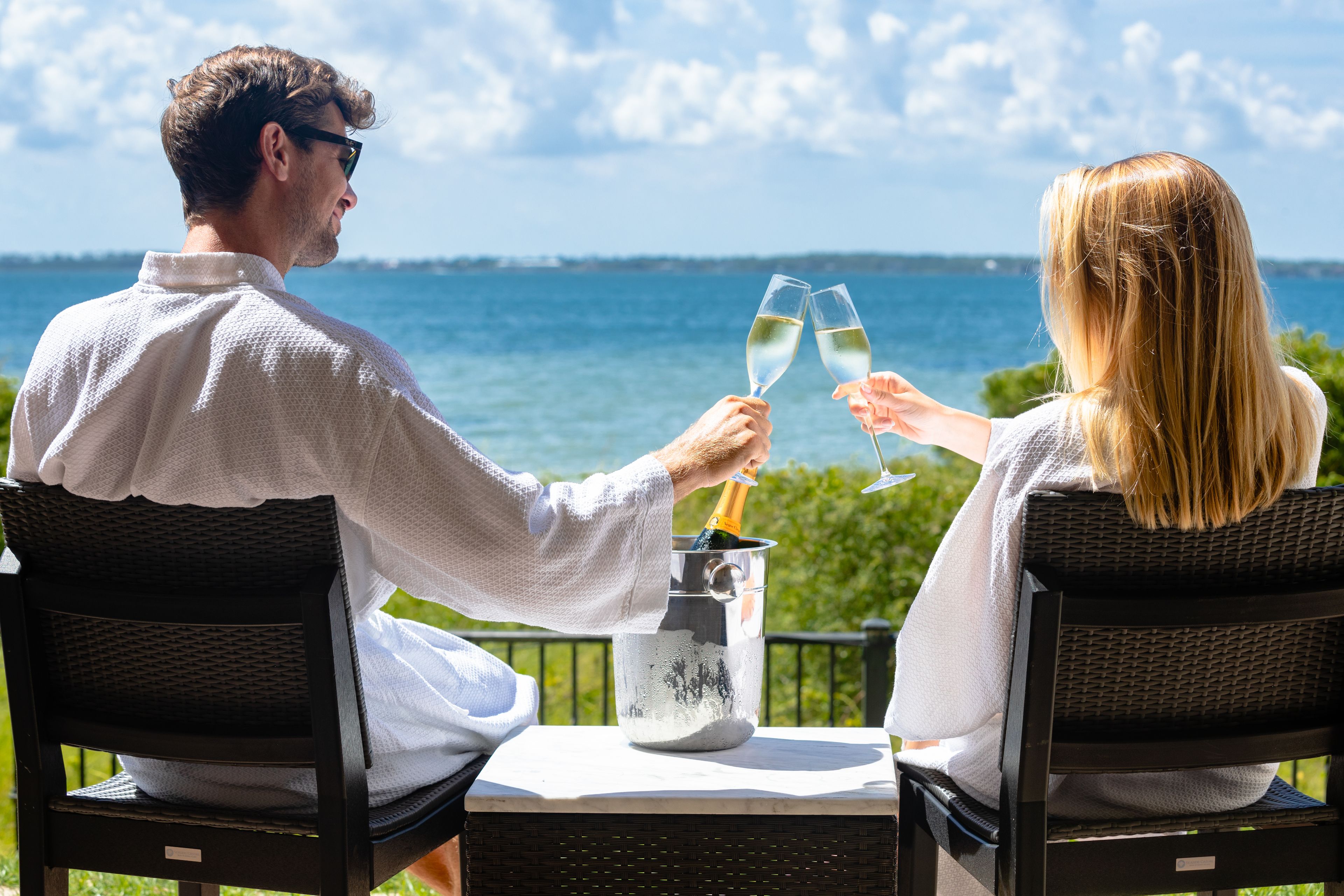 Zwei Personen sitzen an einem Tisch mit Meerblick und halten Champagnergläser.