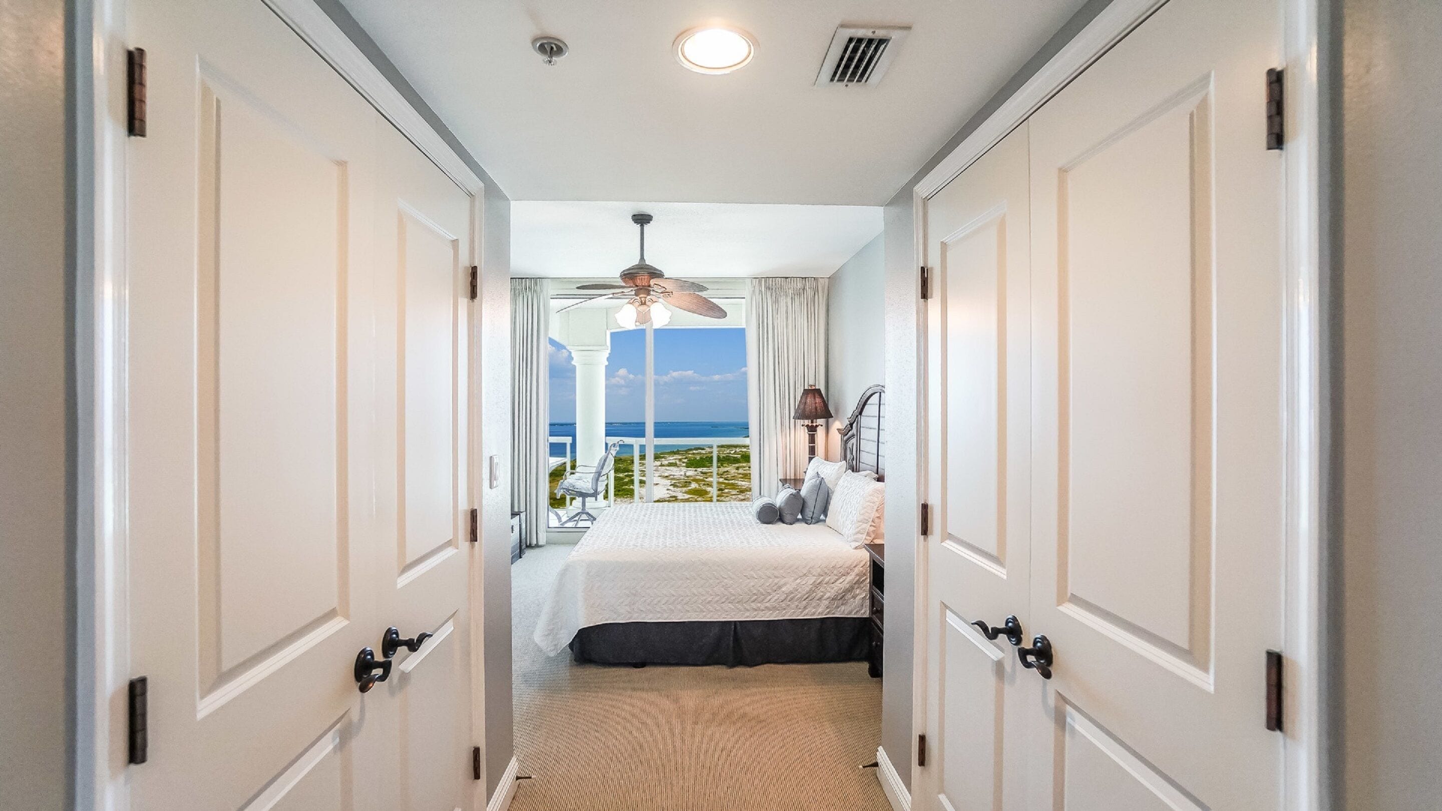 Un dormitorio con cama, ventilador de techo y vista al océano.