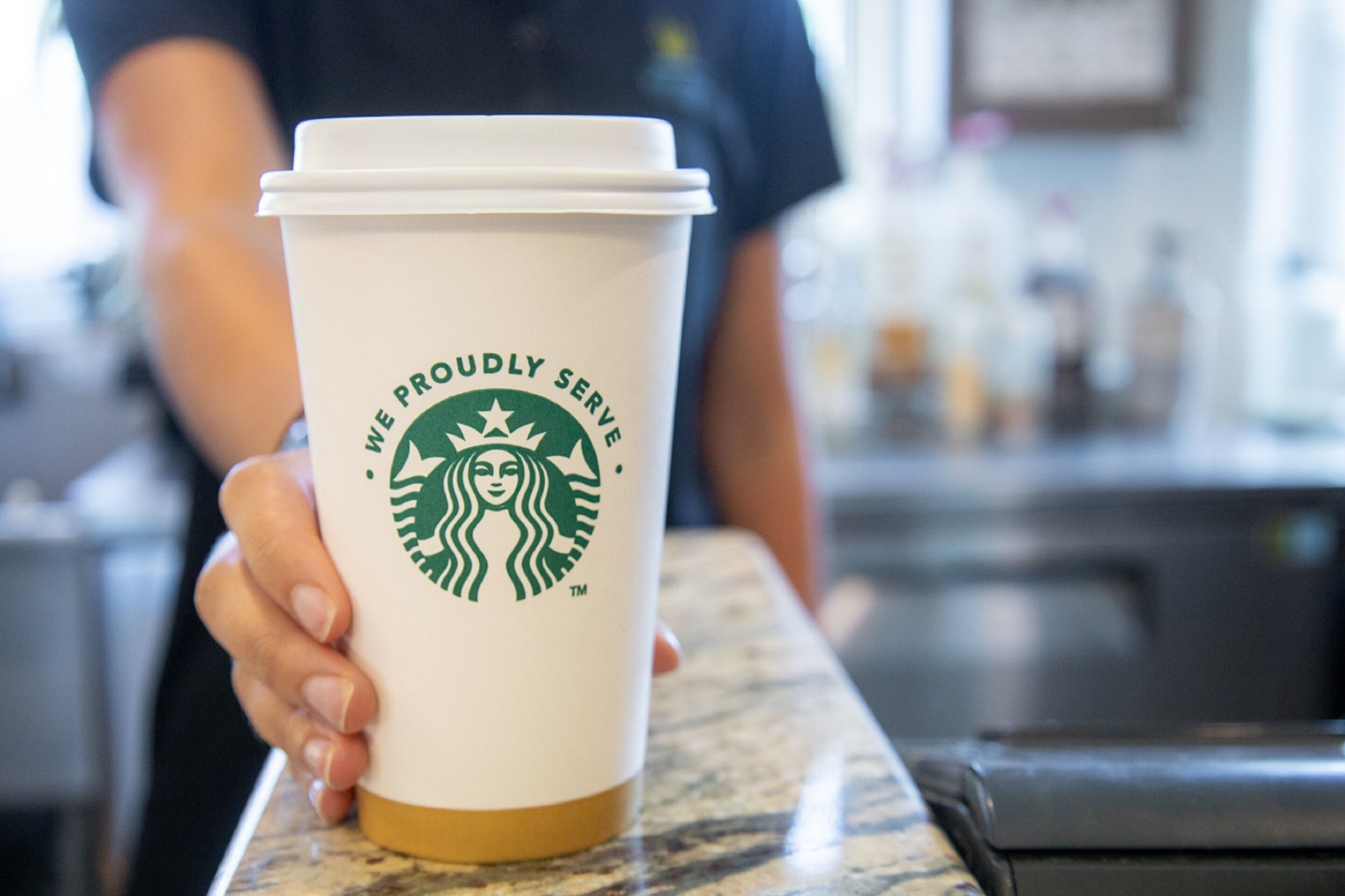 Une tasse Starbucks avec l’inscription « Nous sommes fiers de vous servir » posée sur un comptoir.