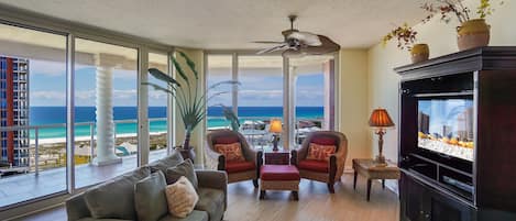Un salon spacieux doté d’une grande fenêtre donnant sur une plage, et aménagé avec un canapé, des fauteuils et un téléviseur.