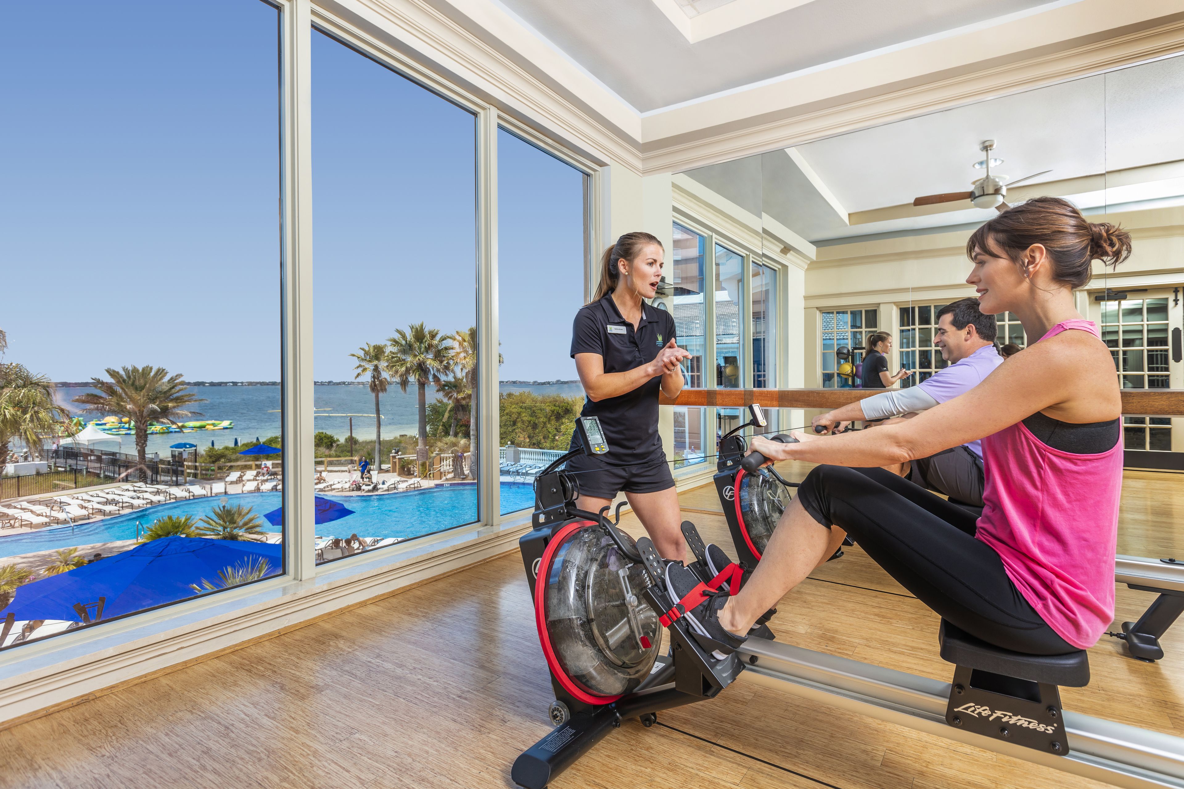 Ett gym med utsikt över en pool och palmer.