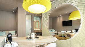 Une chambre d’hôtel moderne dotée d’un coin repas, d’un grand miroir, d’une télévision à écran plat et d’un espace salon confortable.