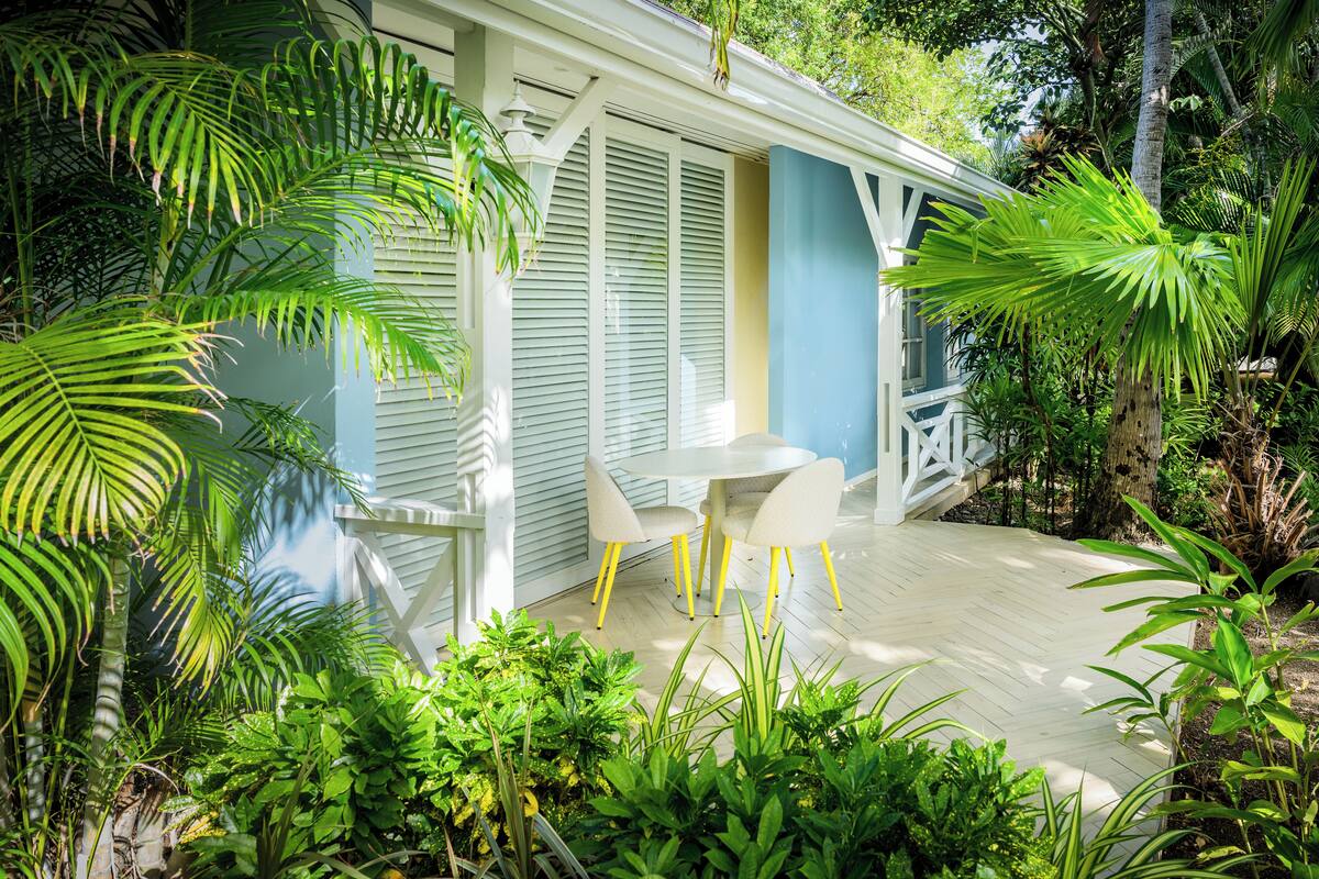 Une terrasse couverte avec une table blanche et des chaises jaunes, entourée d’une végétation tropicale luxuriante.