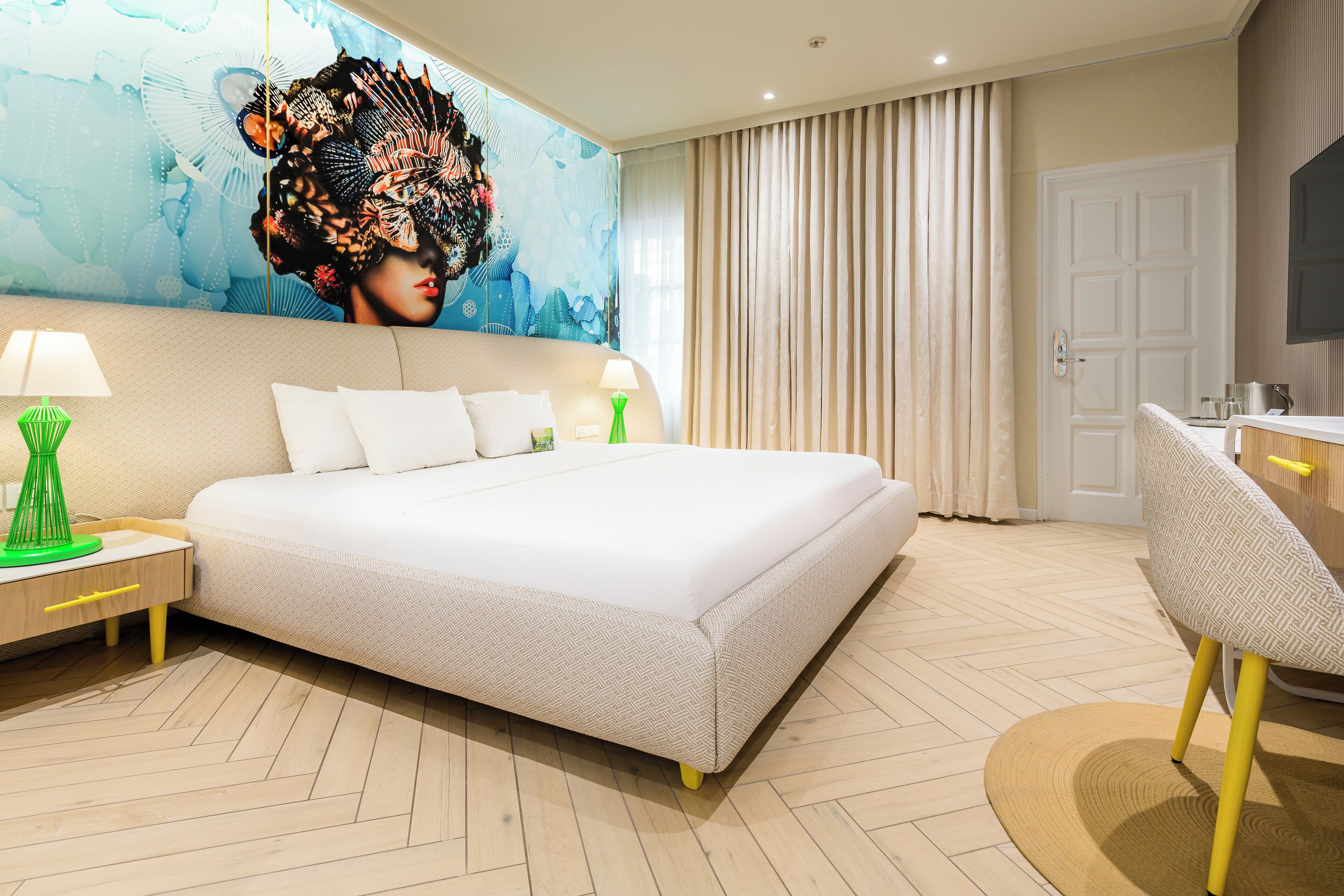 A modern hotel room with a large bed, a desk with a lamp, a chair, and a television on the wall.