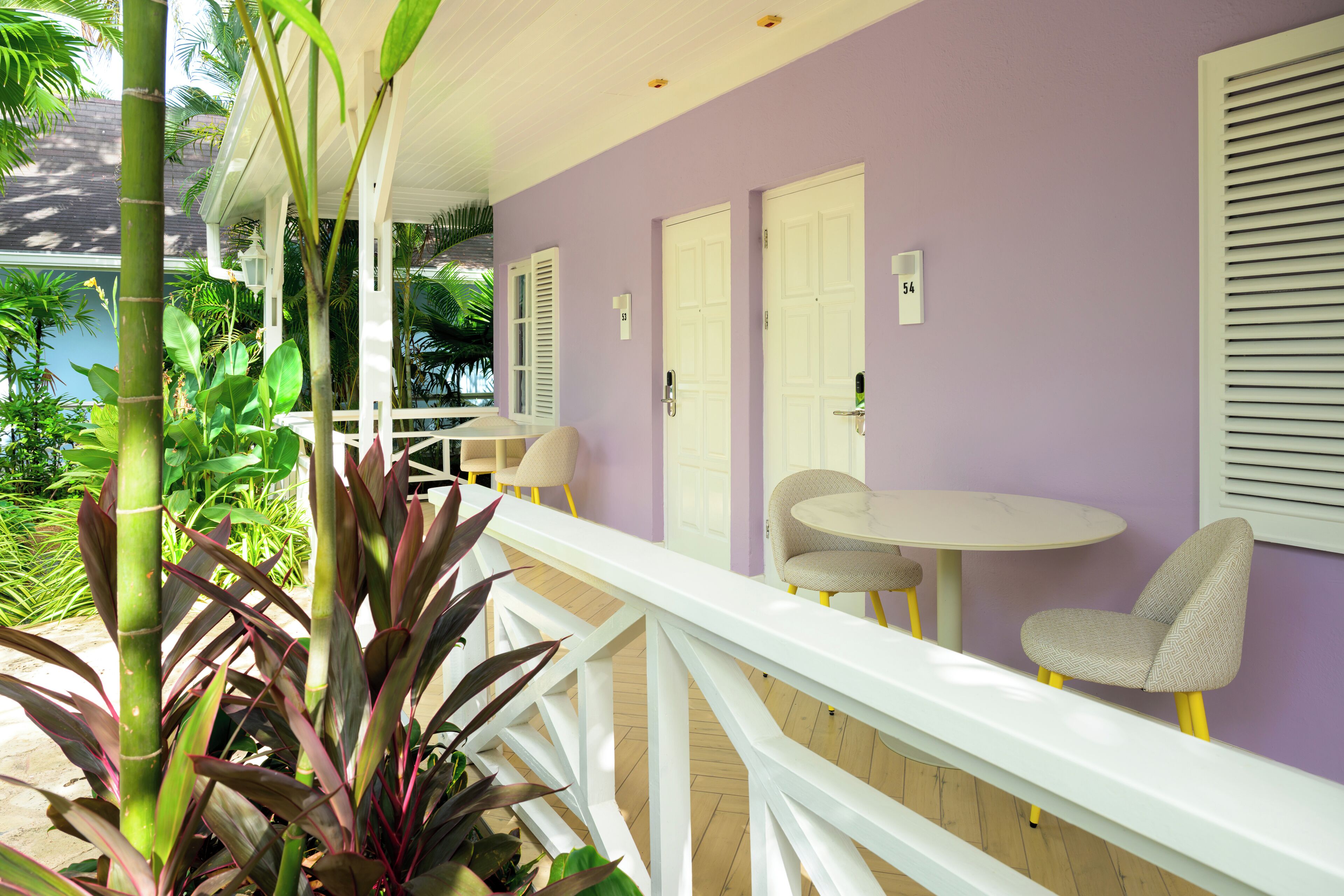 Una habitación con pared morada, puertas blancas, barandilla blanca y una pequeña mesa redonda con dos sillas.