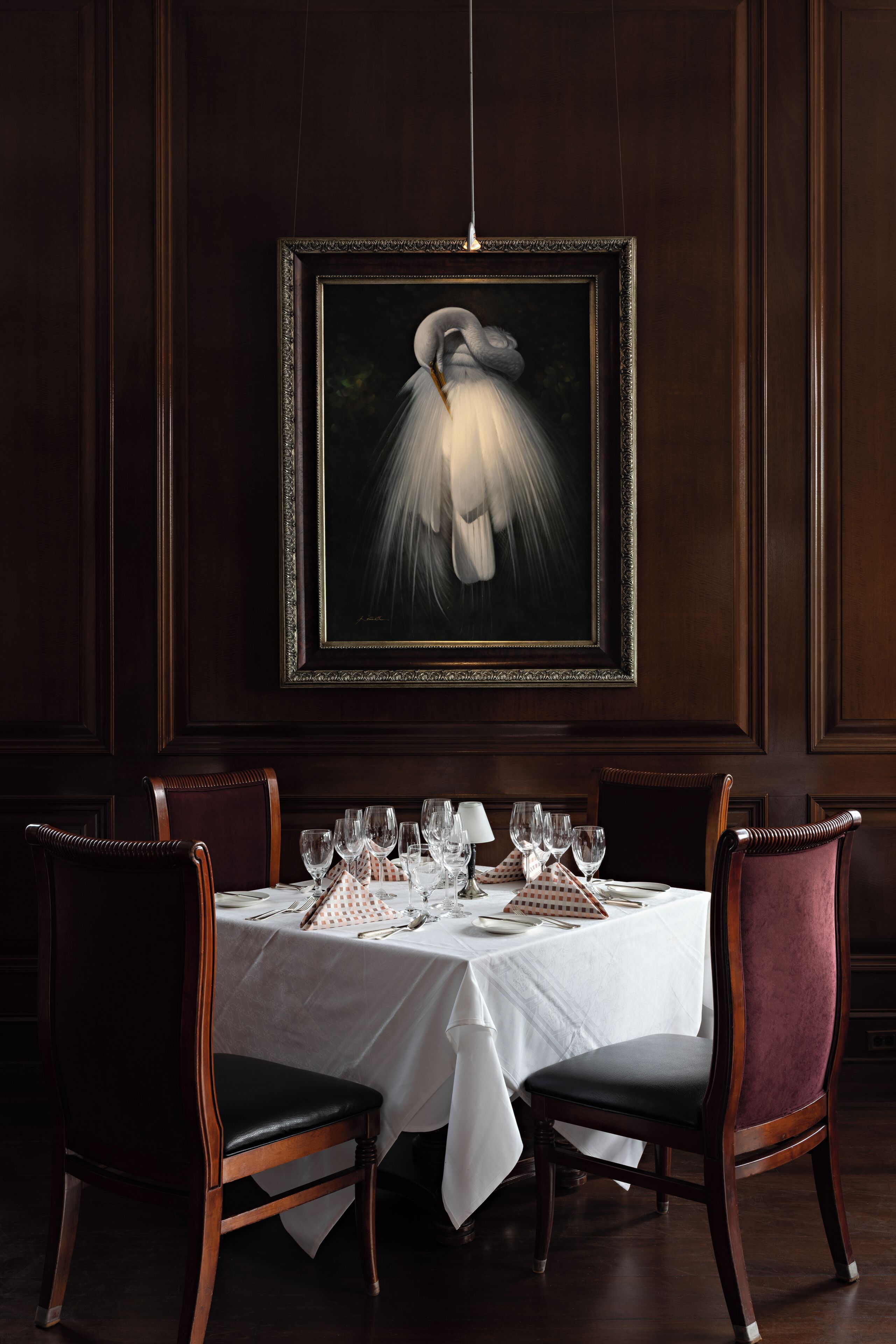 A dining area with a table set for four, framed artwork above, and dark wood paneling on the walls.