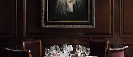 A dining area with a table set for four, framed artwork above, and dark wood paneling on the walls.