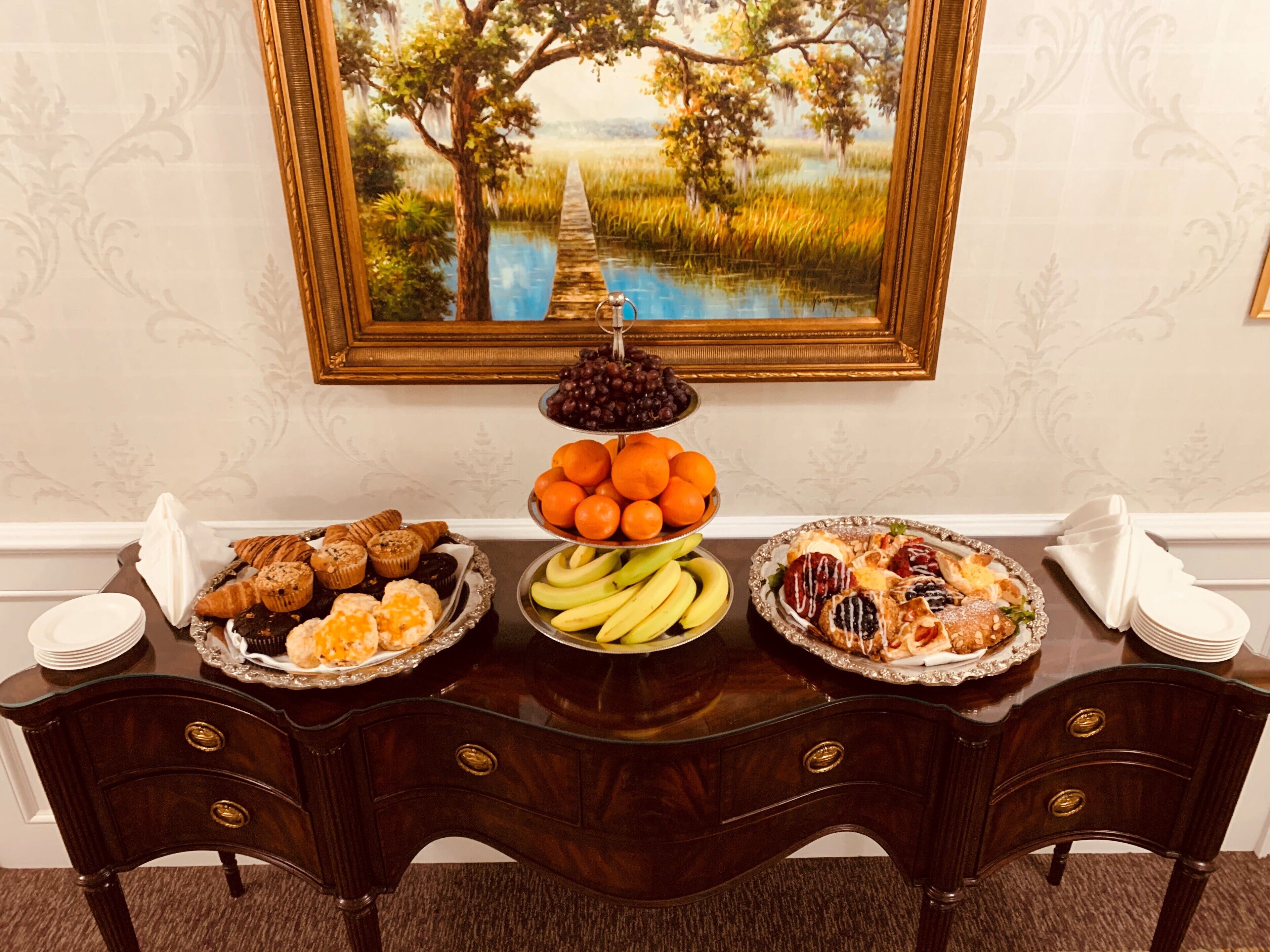 Una mesa de buffet con diversos alimentos, un cuadro en la pared y una mesa de madera oscura.