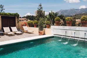A rooftop pool with lounge chairs, potted plants, and a view of mountains.