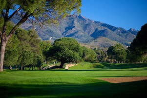 Ein Golfplatz mit Bergblick, Bäumen und blauem Himmel.