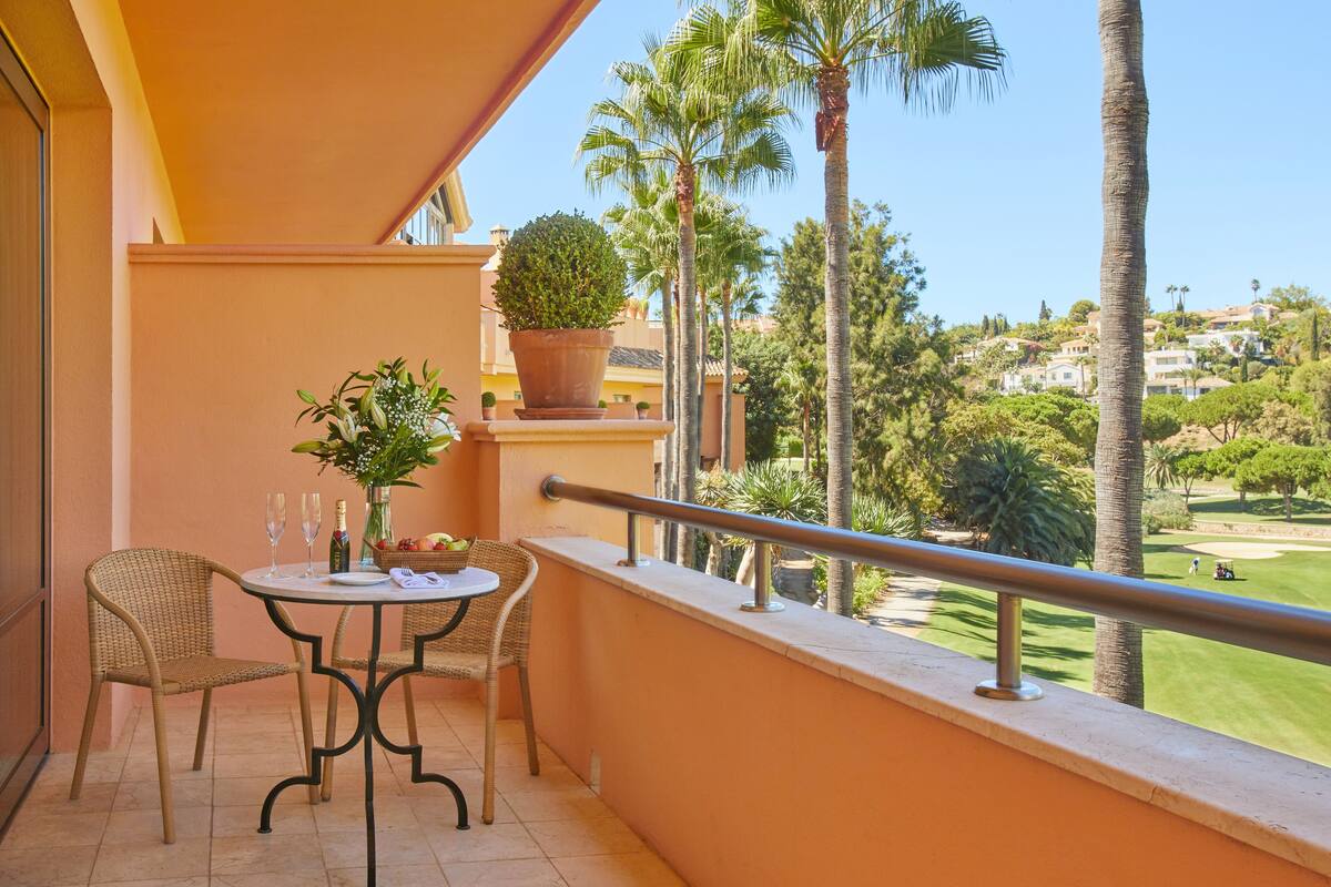 A balcony with wicker chairs, a small table, and a potted plant.
