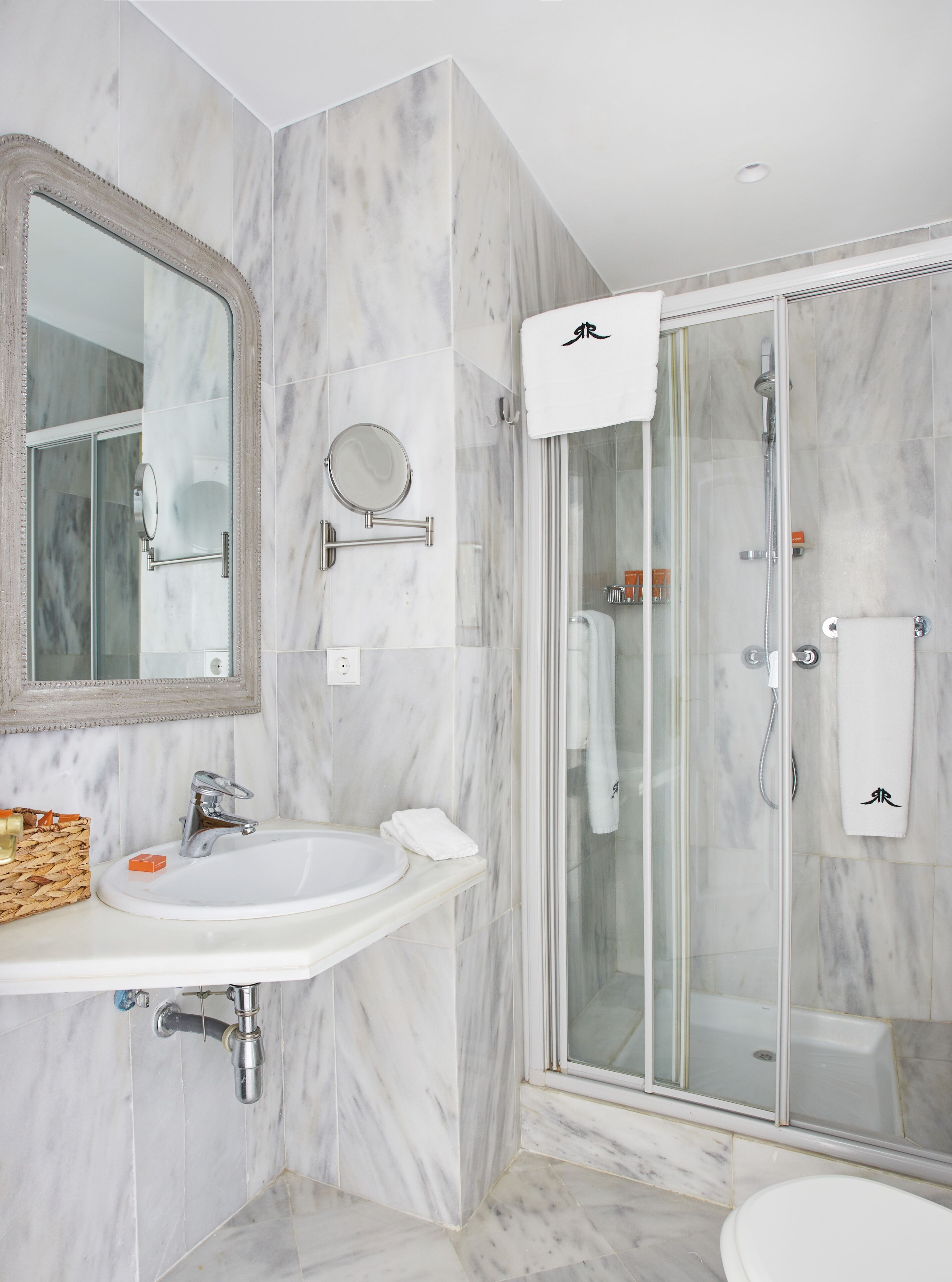 Un baño moderno con lavamanos de mármol, un espejo grande, ducha con cerramiento de vidrio y un inodoro.