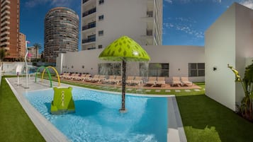 A swimming pool with a green water slide, lounge chairs, and a tropical umbrella.