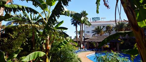 A hotel with a pool surrounded by lush tropical vegetation.