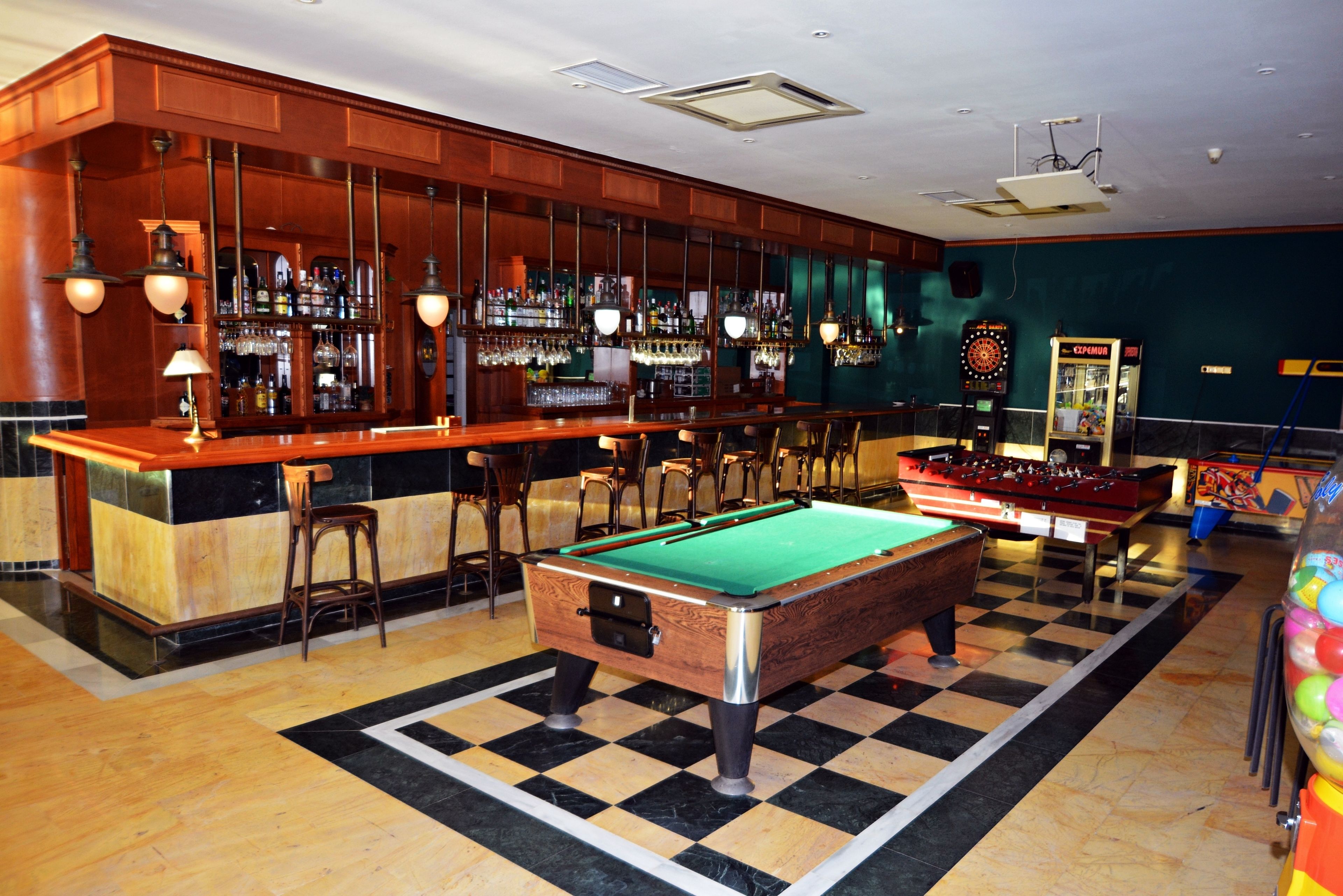 Zona de bar con mesa de billar, taburetes y dardos.