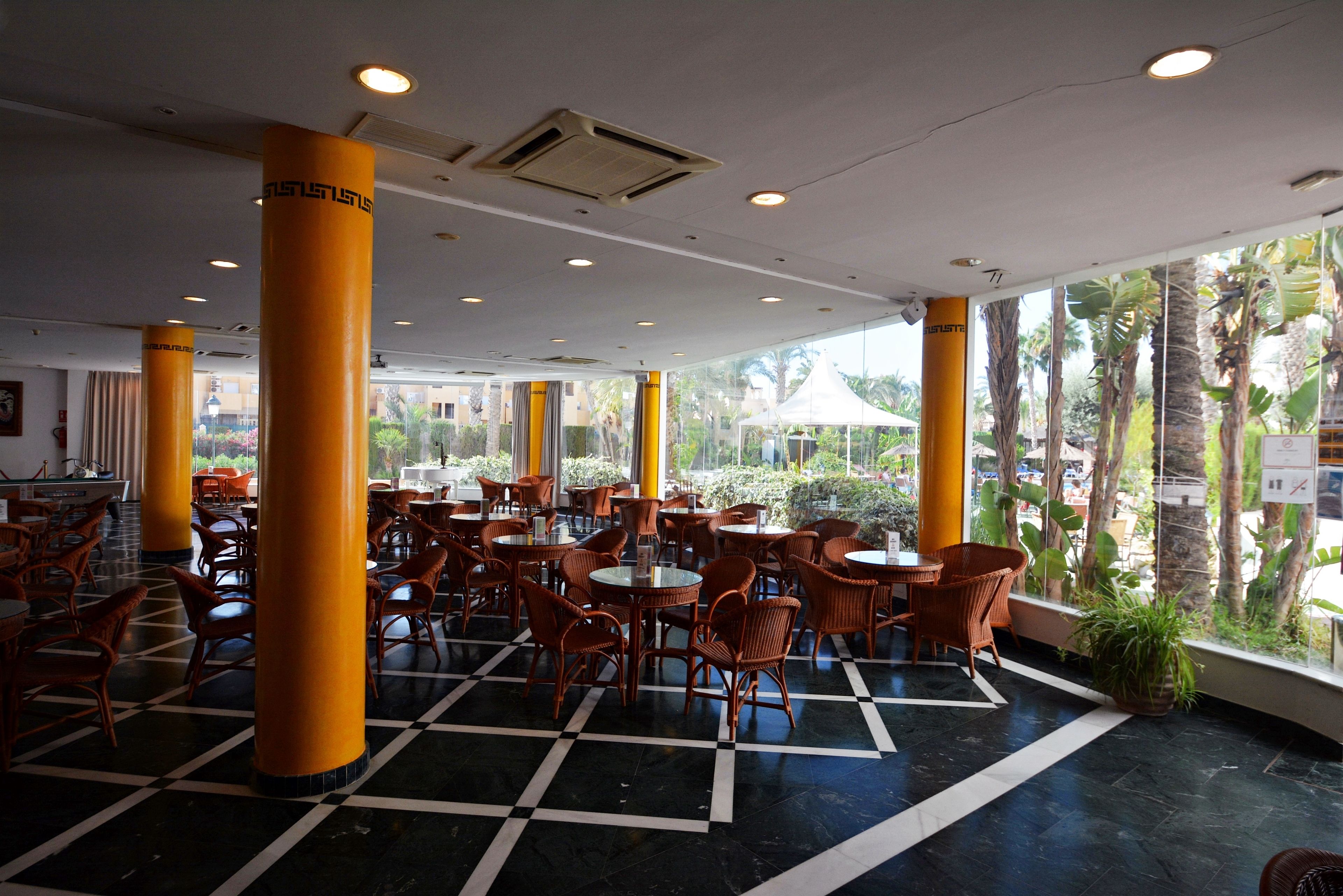 A spacious indoor area with multiple tables and chairs, large pillars, and large windows offering views of the outdoors.