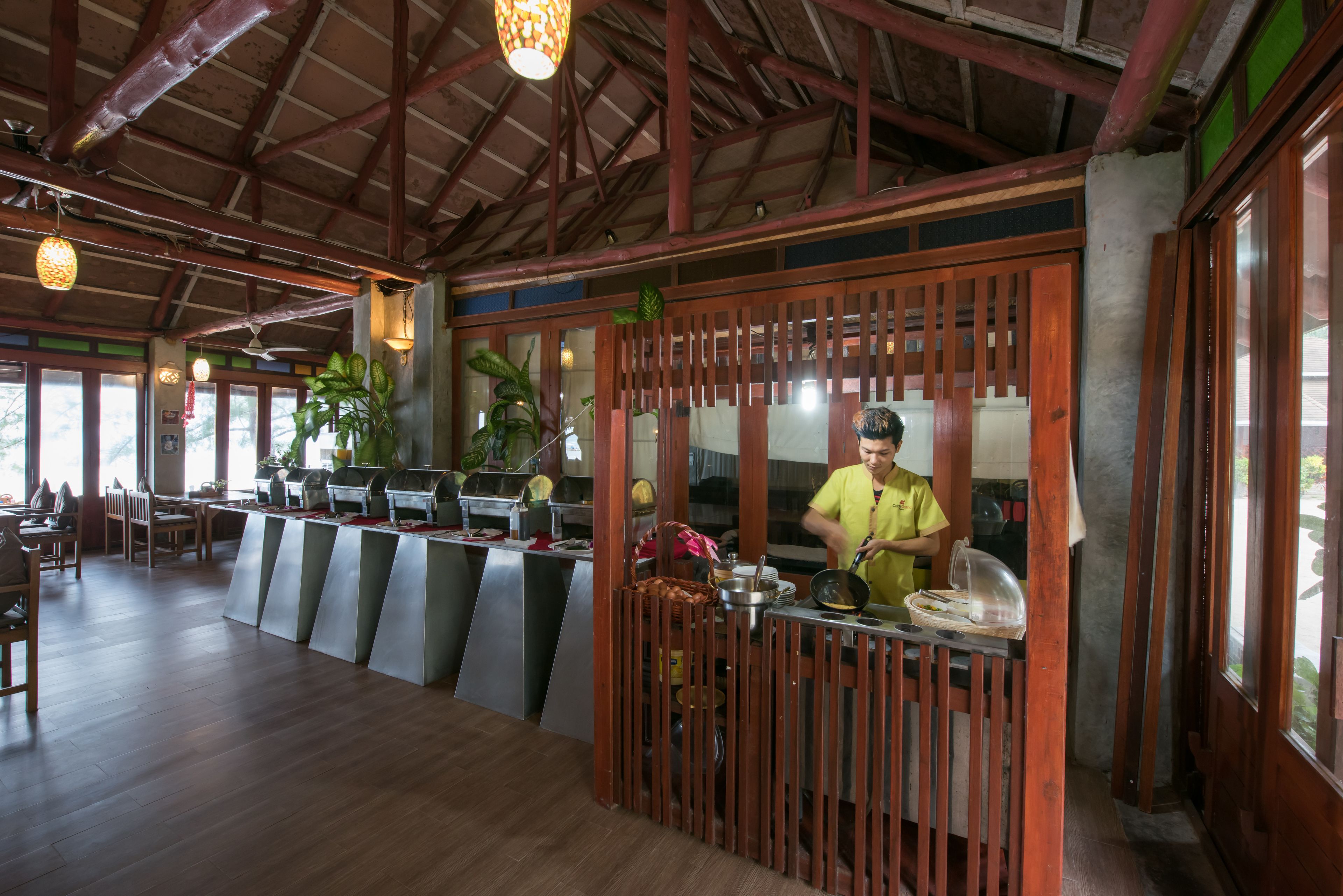 Un restaurant avec un plafond en bois, un comptoir où le chef prépare les plats, et plusieurs tables avec des chaises.