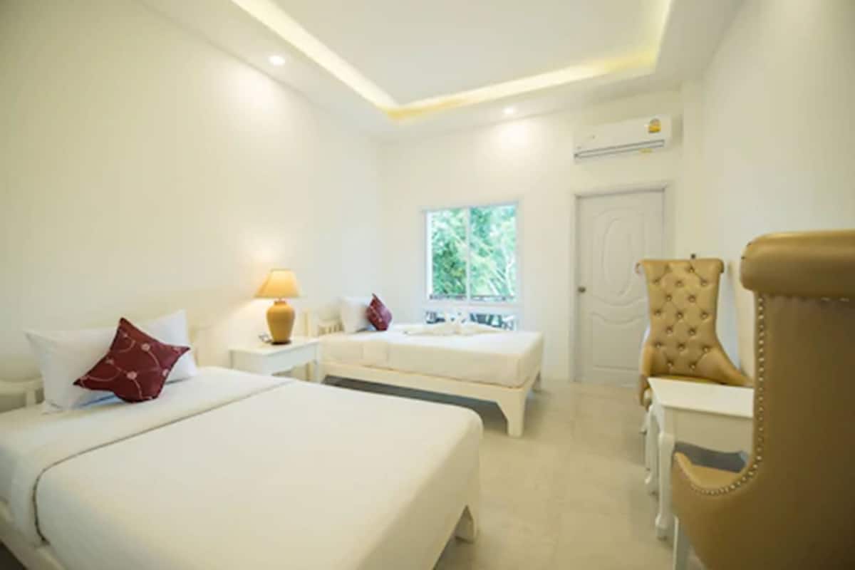 Habitación de hotel con dos camas, una mesita, una silla, un ventanal con vistas a zonas verdes y un equipo de aire acondicionado en la pared.