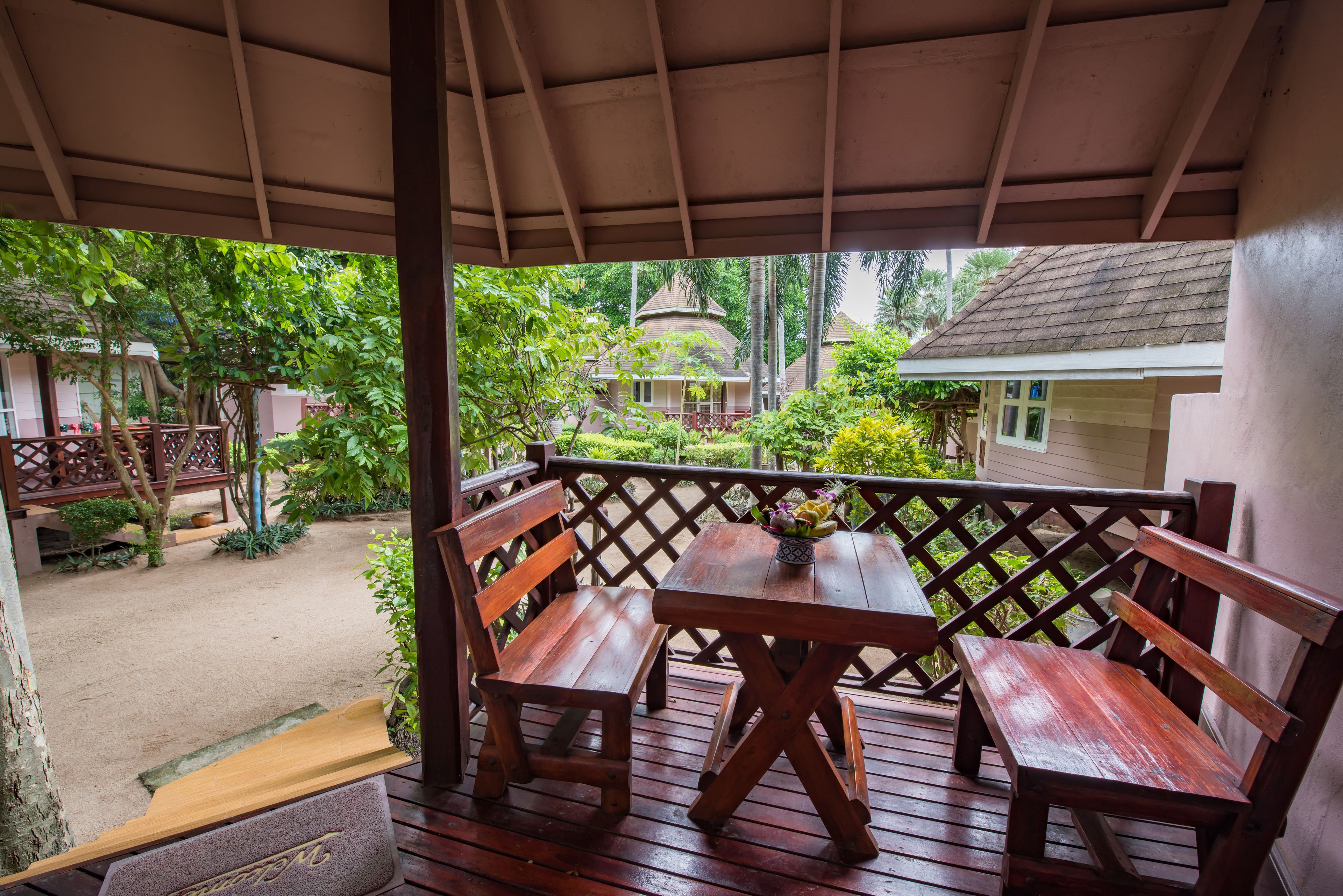 A wooden deck with a table and benches, overlooking a garden with a gazebo and a house.