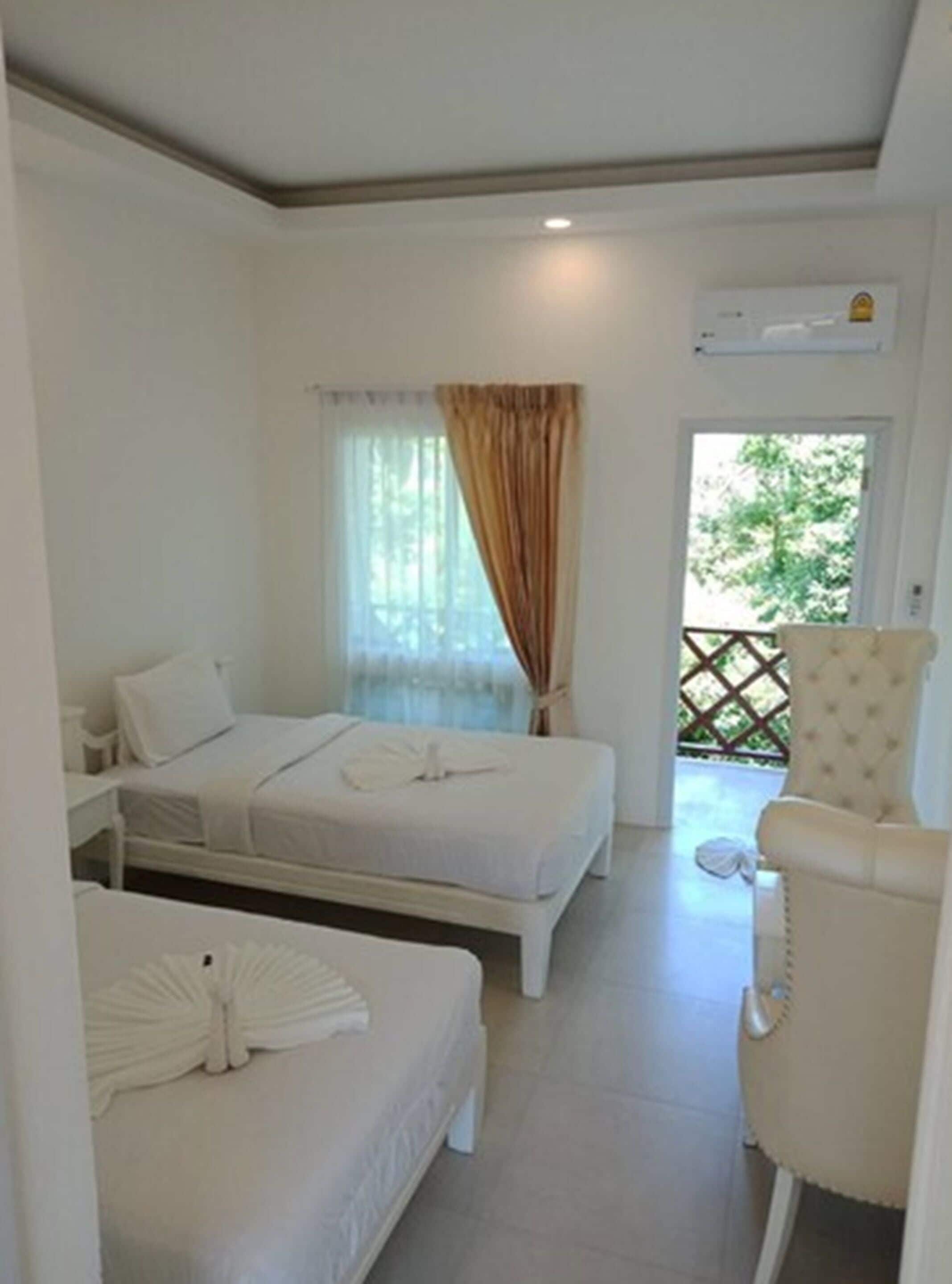 A hotel room with two beds, a sitting area with a chair, and a window with curtains.