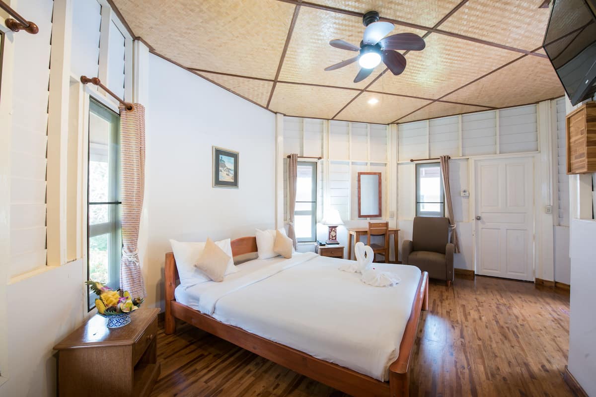 Un dormitorio amplio con una cama grande, techo de madera, ventilador de techo y un escritorio con silla.