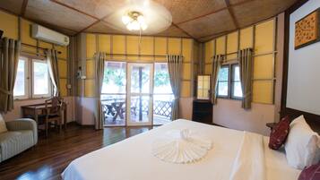 A hotel room with a bed, a desk, and a chair. There is a sliding door leading to an outdoor area.