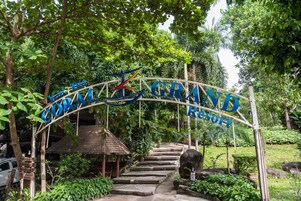Schild für das Kol Tio Grand Resort, mit einer hölzernen Treppe, die davor hinaufführt, umgeben von üppiger Vegetation.
