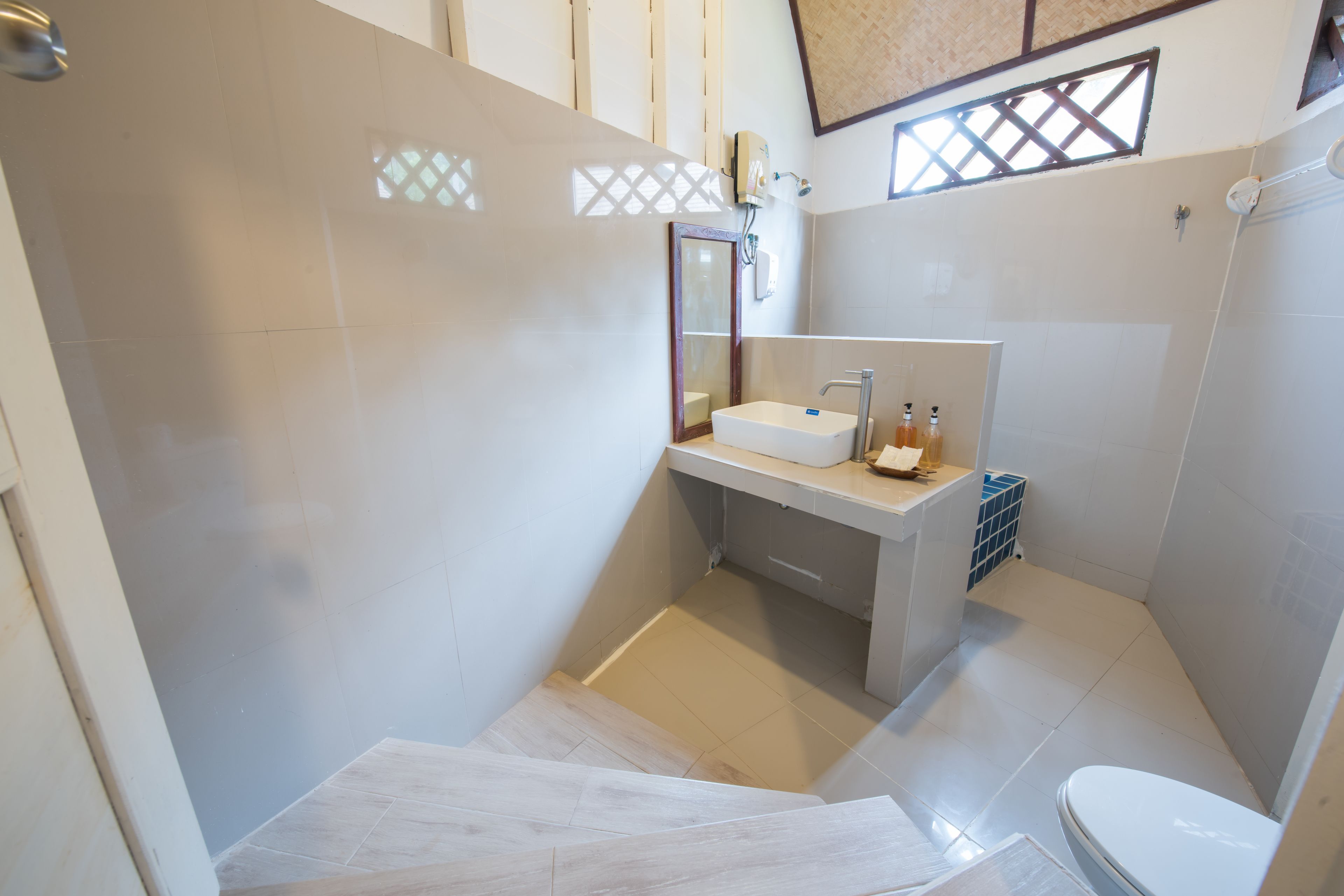 A modern bathroom with a white sink, mirror, and toilet. There is a shower area with a glass door and a small window above the sink.
