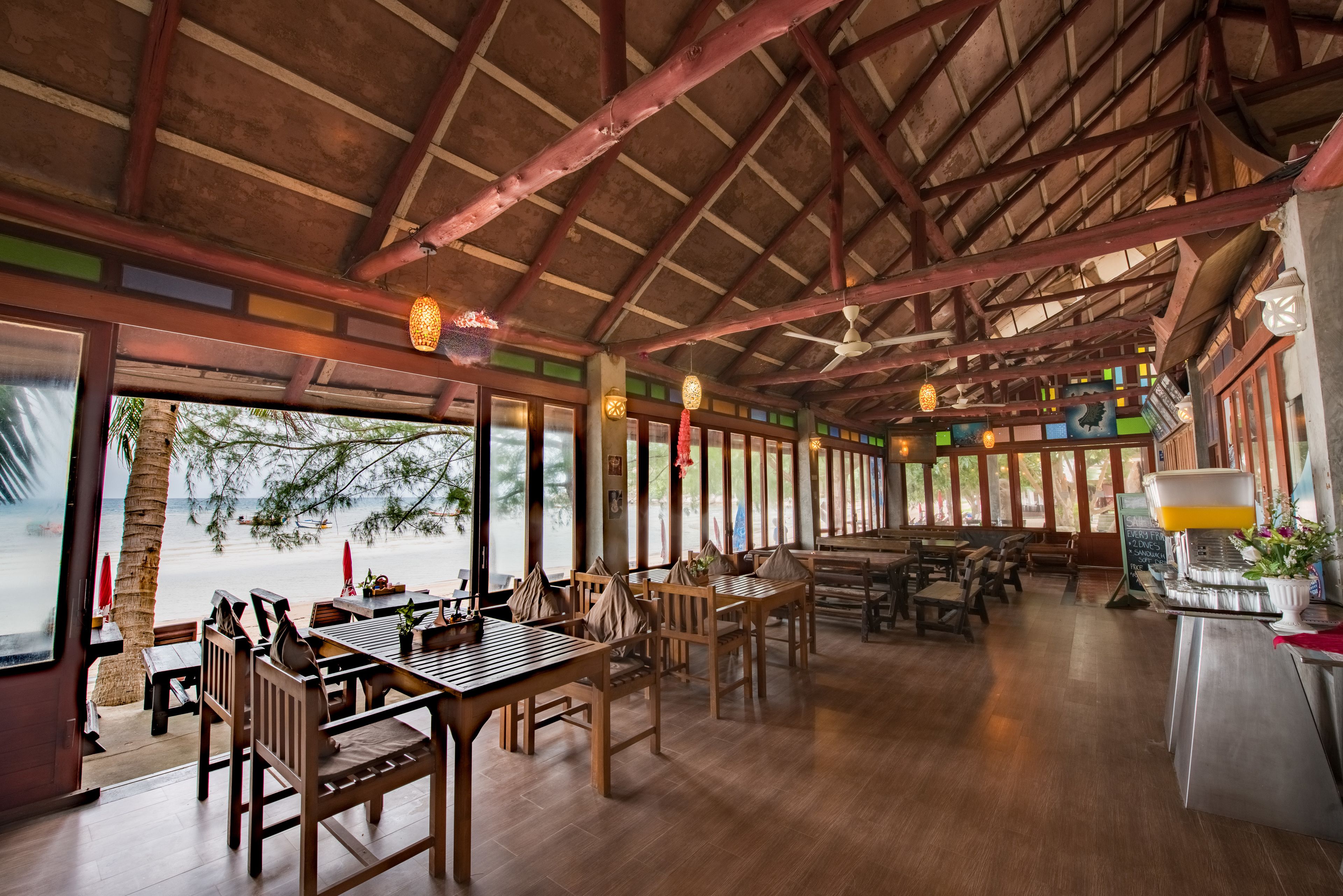 A restaurant with wooden furniture, large windows, and a view of the beach.