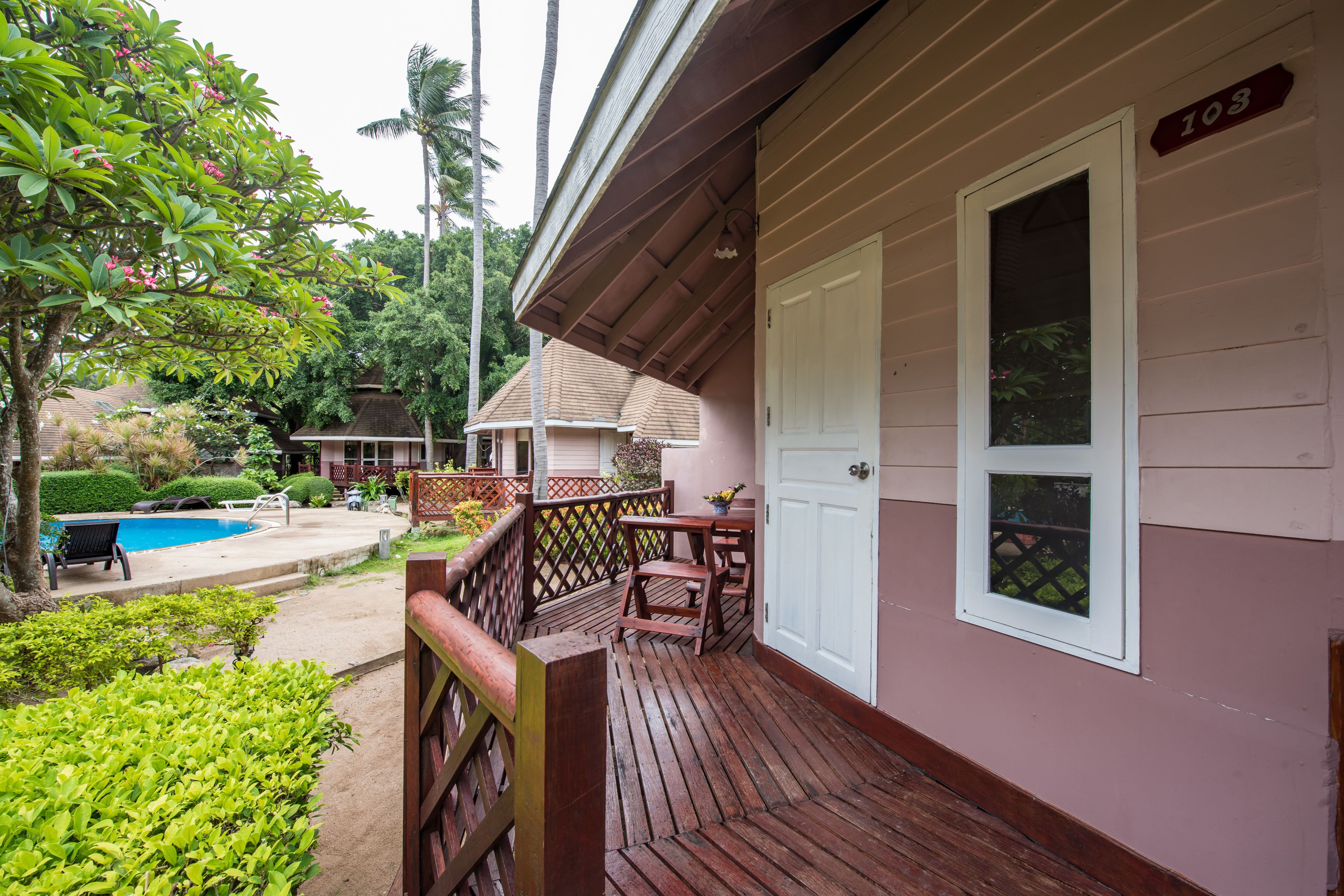 Une terrasse en bois avec une porte blanche, une piscine et une petite maison en arrière-plan.
