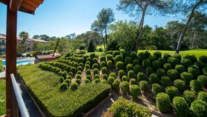 A landscaped garden with neatly trimmed hedges, a pool, and a building with a red roof in the background.