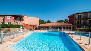A rectangular swimming pool with clear blue water, surrounded by a tiled deck and a covered area with glass walls.