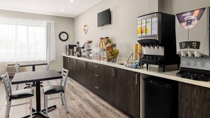 A modern kitchen with a dining area, equipped with a coffee machine, a television, and a clock on the wall. - Super 8 by Wyndham Sarnia ON (Sarnia)