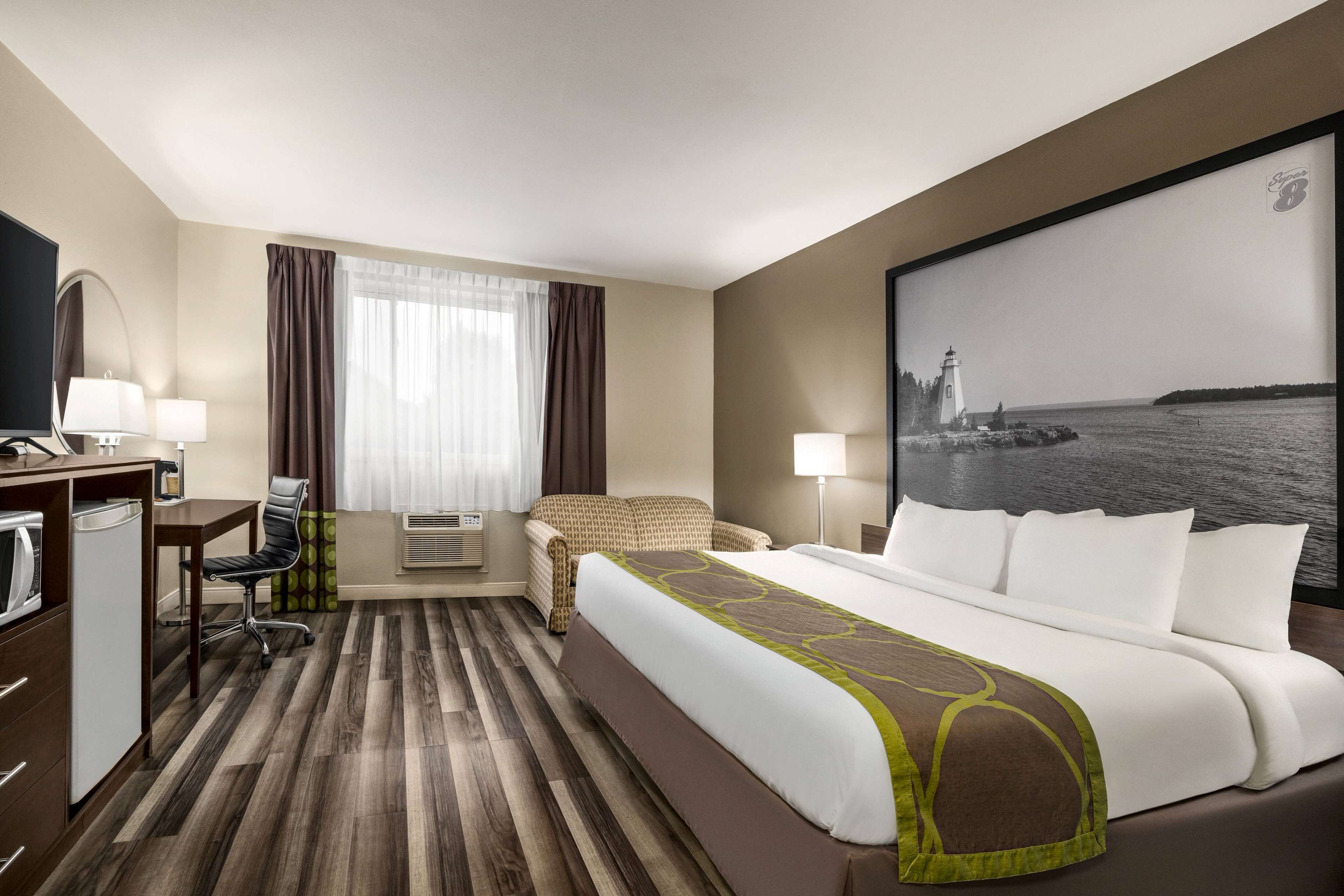Ein Hotelzimmer mit einem großen Bett, einem Schreibtisch mit Stuhl, einem Fernseher und einem Fenster mit Vorhängen.