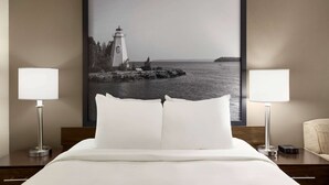 A hotel room with a bed, two bedside lamps, a framed picture of a lighthouse, and a nightstand with a clock. - Super 8 by Wyndham Sarnia ON (Sarnia)