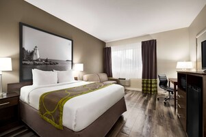 A hotel room with a large bed, a desk, a chair, a TV, and a window with curtains.