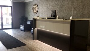 A reception area with a wooden floor, a black reception desk, a black leather chair, a wall clock, and a signboard. - Super 8 by Wyndham Sarnia ON (Sarnia)