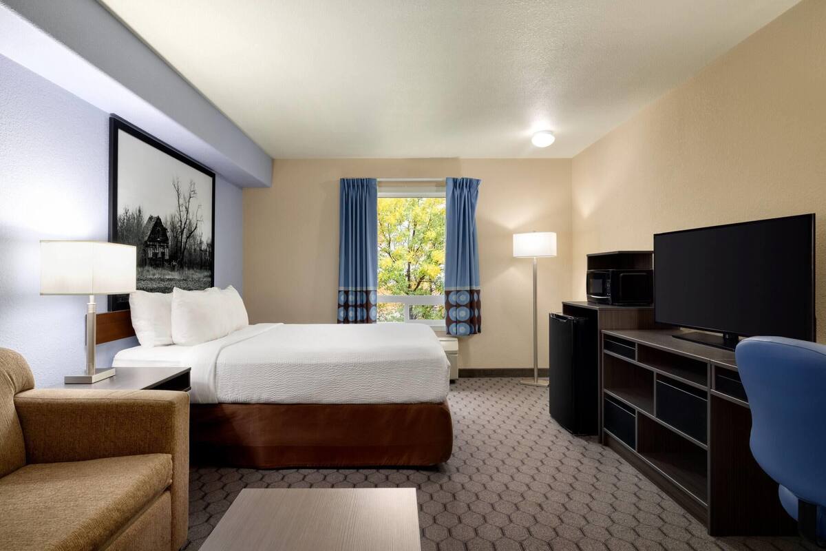 Une chambre d’hôtel avec un lit, un bureau, une télévision, un canapé et une fenêtre avec des rideaux.