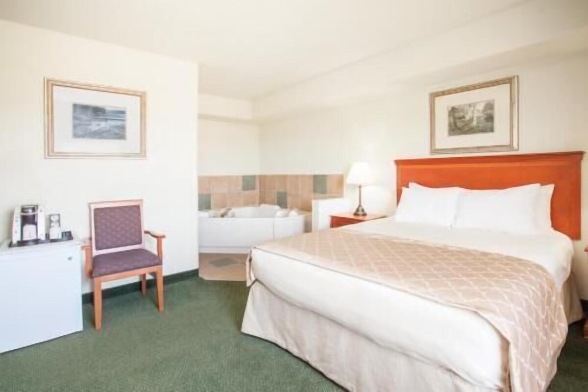 Hotellihuone, jossa on sänky, tuoli, lamppuvarusteinen työpöytä ja taulu seinällä.