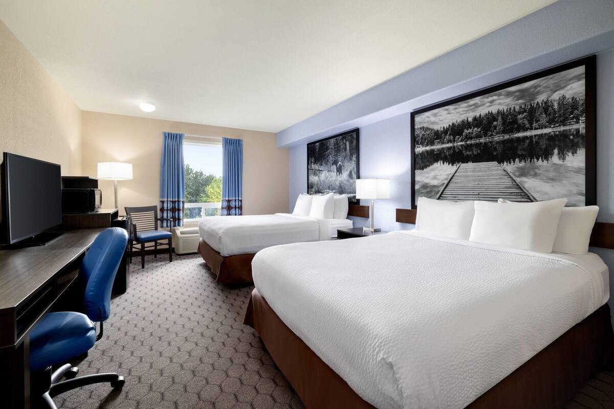 Une chambre d’hôtel avec deux lits, un bureau avec un ordinateur, une chaise et une grande fenêtre avec des rideaux.