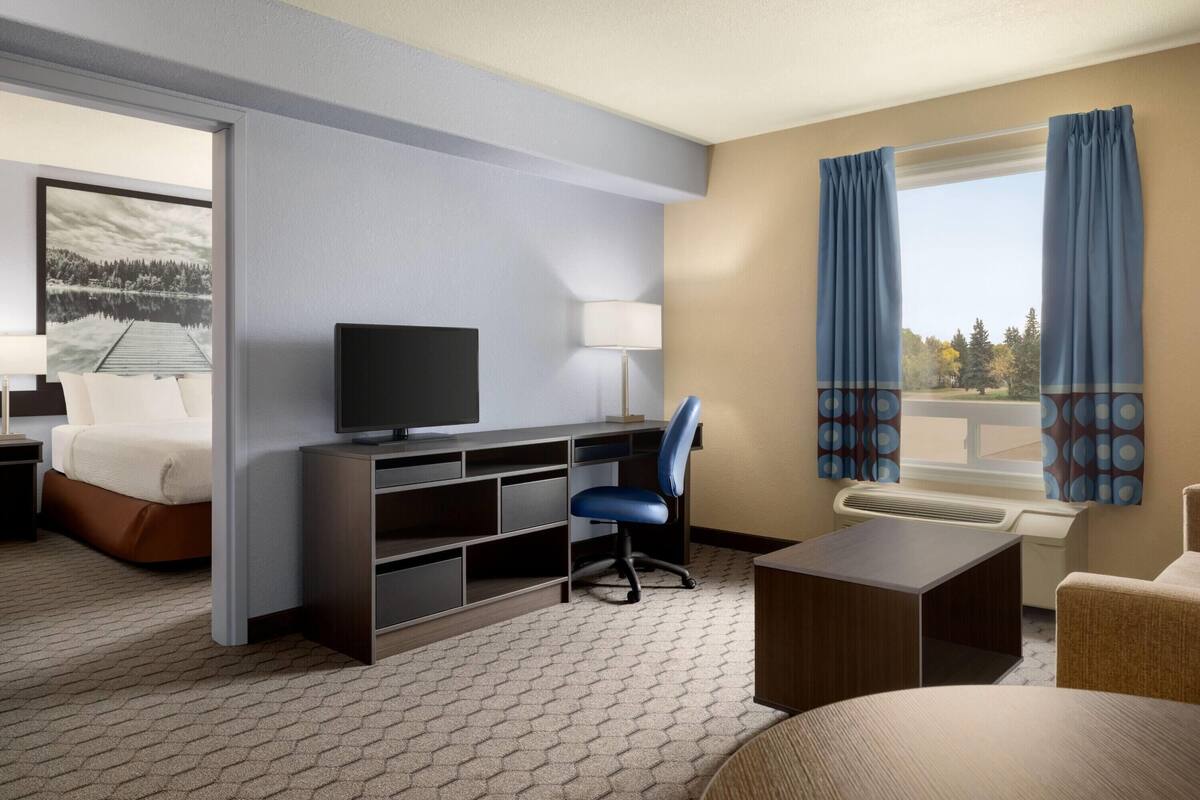 Une chambre d’hôtel avec un lit, un bureau, une chaise, une télévision et une fenêtre avec des rideaux.