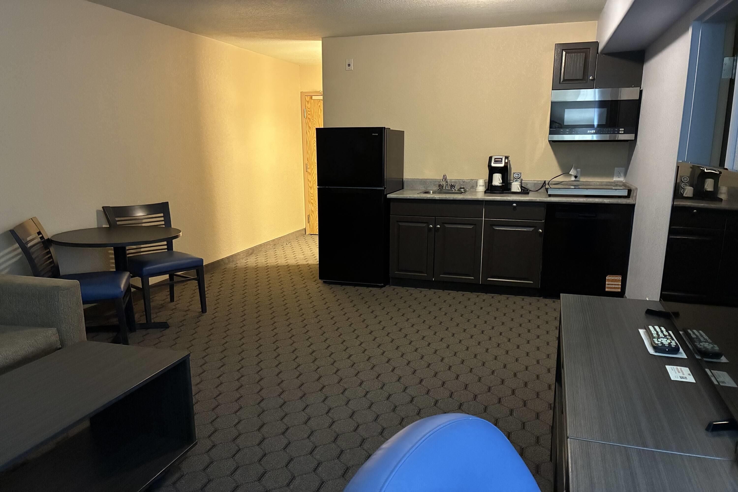 A compact hotel room with a kitchenette, a dining area with a table and chairs, and a small seating area with a sofa.