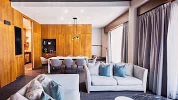 Een moderne woonkamer met een bank, een eethoek met tafel en stoelen, een keuken op de achtergrond, en een groot raam met gordijnen.