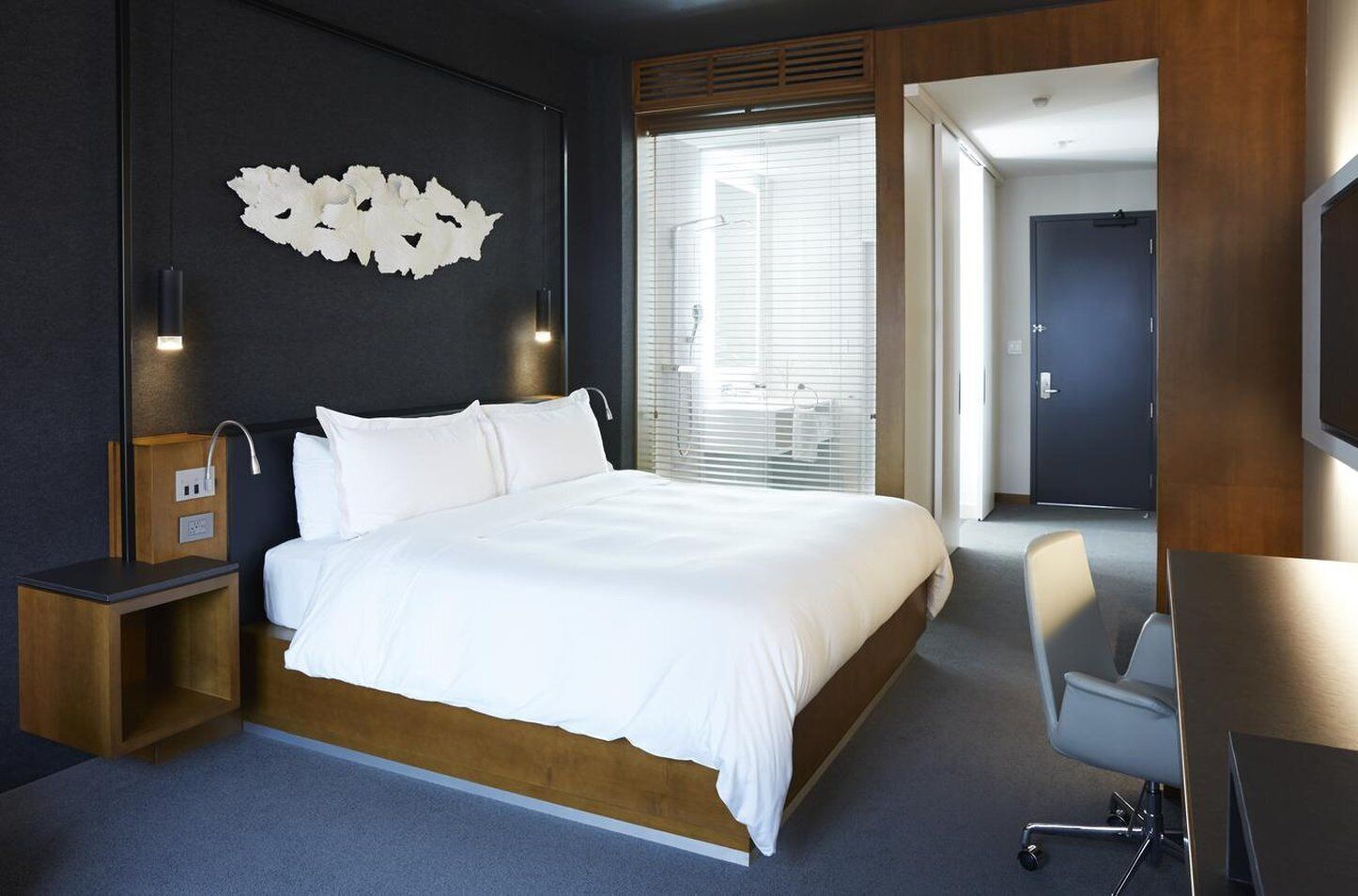 A modern hotel room with a large bed, bedside tables, a desk, and a chair.