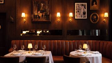Een restaurant met houten lambrisering, een zitgedeelte met hoge banken, en tafels gedekt met wijnkannen en borden.