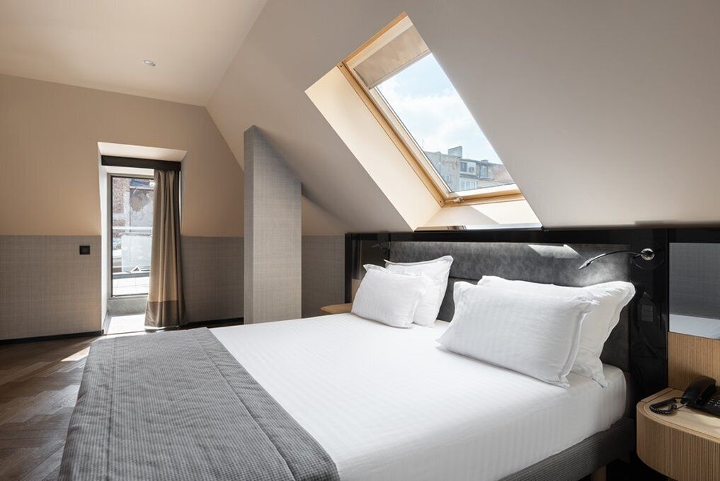 Quarto moderno com claraboia, cama com roupa de cama branca e mesa de cabeceira de madeira.