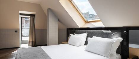 Quarto moderno com claraboia, cama com roupa de cama branca e mesa de cabeceira de madeira.