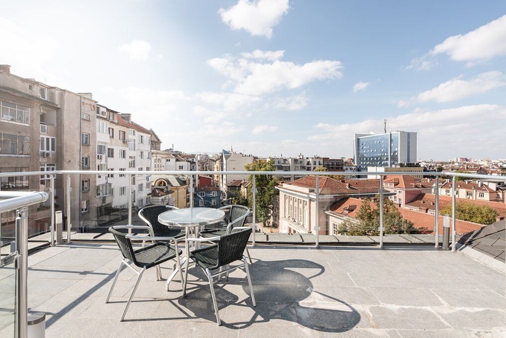 A rooftop terrace with a table and chairs, offering a view of the cityscape.