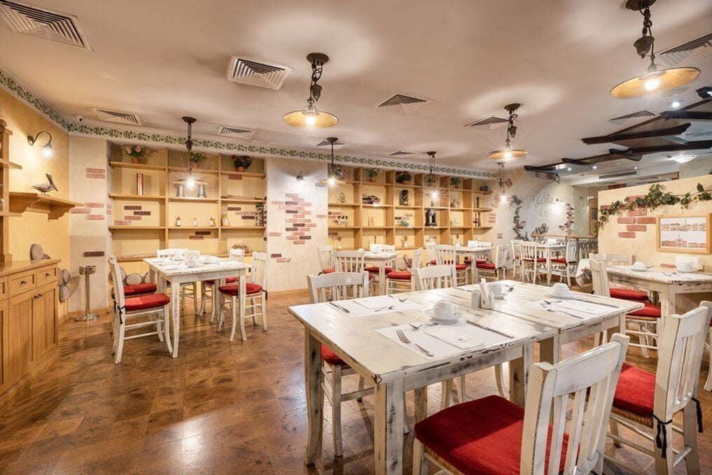 Un restaurante con mesas blancas y sillas rojas, estantes de madera con varios objetos y ventiladores de techo.