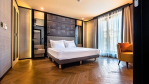 Een moderne hotelkamer met een groot bed, een zithoek met een stoel, een kaptafel en een groot raam met gordijnen.